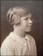 Head-and-shoulders photograph of a young girl. She wears a light-coloured blouse and faces right, looking out of the picture, with a slight smile. Her short hair is pulled back from her face and pinned up.