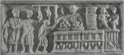 This is a market stall selling food and drink in Rome. A merchant stands near bowls of fruit and a tall, dense basket used to hold live snails. This marble relief was found on a Roman funerary stele dating to approximately the second century C.E.