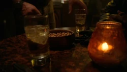 Two glasses of ginger ale at a bar table (among a bowl of nuts and a candle).