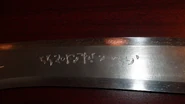 A close up of "Honor in Death" written on Tyre's sword in Satedan lettering.[4]