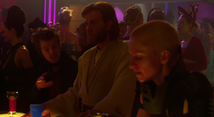 A shot from Attack of the Clones shows Nyrat Agira stood talking with two other Outlander Club patrons behind Obi-Wan Kenobi, Elan Sel'Sabagno, and Kalyn Farnmir, who are stood at the club's bar.