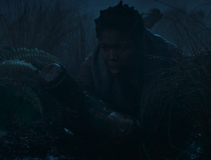 Laying on her stomach in the muddy undergrowth of Yavin 4, Snee stares in horror at the severed foot of Crab, still in its boot, as she holds it up.