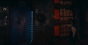 Guthan Archi hurls a rock at TT-8L-OT's head shield while the droid is retracted inside the Olega Jedi temple wall beside a shielded doorway.