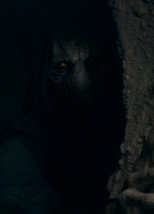 Hidden in shadow, Darth Plagueis peers around a rocky corner.