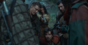 Crab and Rowd stand either side of Cassian Andor holding him by the arms as he kneels before Gerdis and Bardi. Behind the prisoner, Tick aims a blaster pistol at his head.