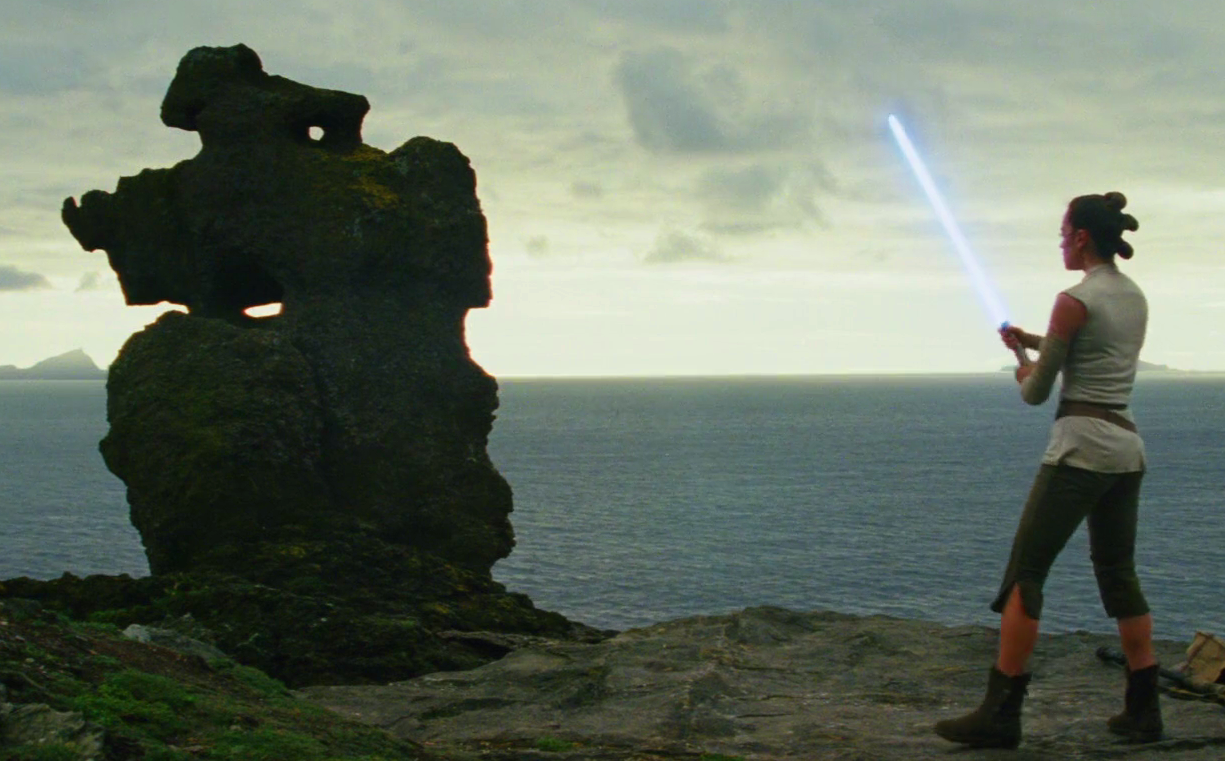 Rey practices using her lightsaber with a large rock.