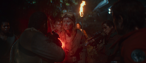 Lit by torches at night on Yavin 4, Crab shoots Rika in the chest with a blaster rifle as Snee, Rowd, Bardi, Musk, and Cassian Andor watch.