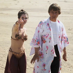 Carrie Fisher, in this costume, points directly towards the camera while Mark Hamill, in a white floral robe, looks taken aback.