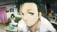 Itaru sitting at his desk while Okabe talks with Alpacaman.