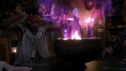 Clea sets a fire ablaze beneath a cauldron