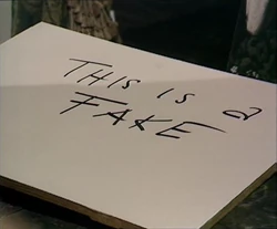 The Doctor writes "THIS IS A FAKE" on the boards  would use to paint six copies