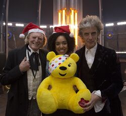 Pudsey with David Bradley (the First Doctor), Pearl Mackie (Bill Potts), and Peter Capaldi (the Twelfth Doctor) on the set of TV: Twice Upon a Time.