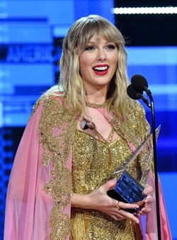 Taylor Swift is looking away from the camera, smiling, and holding an award.