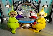 The Teletubbies are sitting at the Tubby Table with some Tubby Toast.