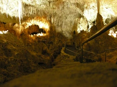 A picture of a partially illuminated cave with a jagged rock ceiling and a walkway extended into the cavern.