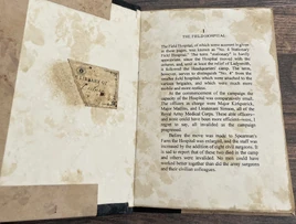 A copy of Sir Frederick Treves "The Tale of a Field Hospital" opened to the first page. The book is covered in various brown stains. Opposite the first page is a torn bookplate reading "Library of Leitner".