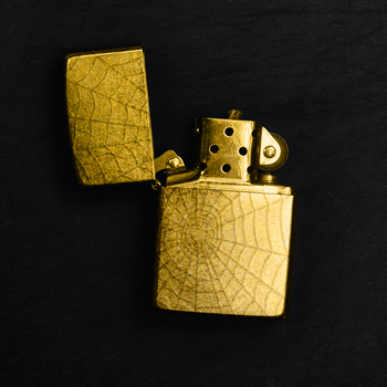 Photo of a golden lighter with a spiderweb pattern.