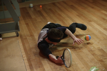 Noah, blindfolded, tries to hit the balls with a tennis racket.