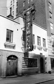 A black and white photograph of the Stonewall Inn, showing half of a sign that was placed in the window by the Mattachine Society several days following the riots