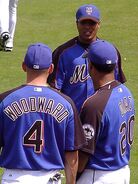 The 2005-2006 spring training uniform which has the blue in front with the black covering the arms. With the black is the orange piping that only appears on the front. On the front it has 2 black lines creating sleeve panels and on the left sleeve is the dark version of the Mets patch with no patch on the right.