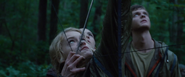 Glimmer attempts to shoot Katniss with a bow