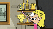 S5E22A Lola replaces the family photos on the shelf with her pageant trophies