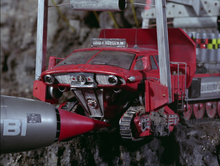 Thunderbird 1's red nosecone props up a truck as it balances on the edge of a cliff