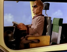 The Hood at the controls of a plane; we see him through a side window