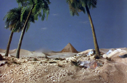 The Sahara Desert; three palm trees framing a distant pyramid in the background
