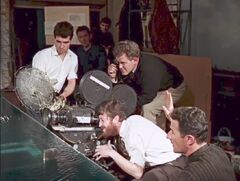 Foreground to background: Derek Meddings (bottom right, raising his hand), Jimmy Elliott (in white shirt, on camera), Michael Wilson (in black top), Ron Ashton (in white shirt). Behind Ashton is Steve Mattick, and behind Mattick is Brian Johnson.