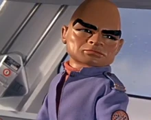 The Hood, wearing a blue tunic, looking behind him and frowning