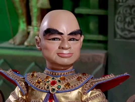 A bald man with thick eyebrows, wearing an elaborate jeweled ceremonial outfit