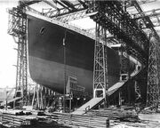 Photograph of a huge gantry with the bow of a large ship that has been painted in dark colours.