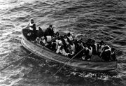 Photograph of a lifeboat, filled with people wearing life jackets, being rowed towards the camera.