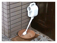 A watering can placed at a strange angle between a bowl and a door.