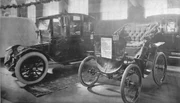 An electric vehicle and an antique car on display at a 1912 auto show