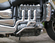 Closeup picture of a motorcycle engine with three heavily chromed exhaust pipes coming out of the side