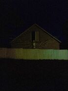 The Angel standing in front of a house at night.