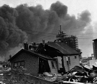The Man With The Upside-down Face is standing in a badly damaged house.