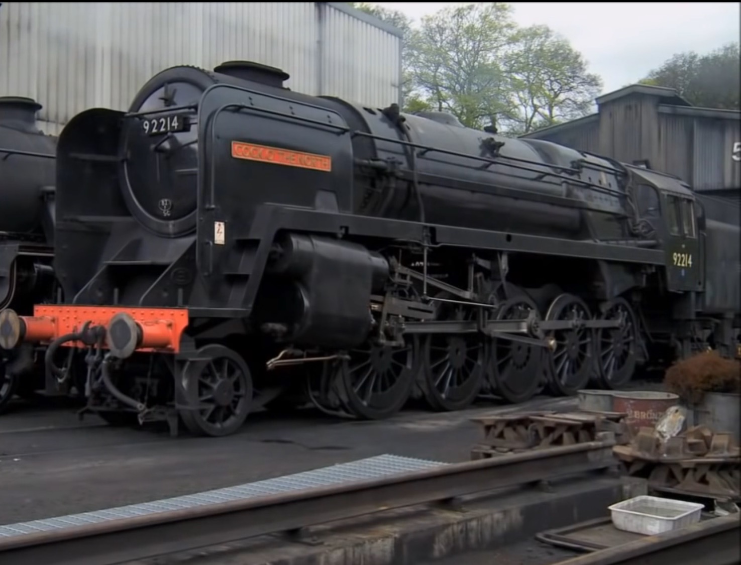 A logging locomotive and tender round the bend past an old water