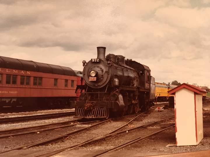 A logging locomotive and tender round the bend past an old water