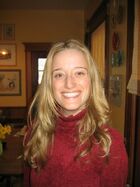 A young caucasian woman with blond hair and a red turtleneck sweater smiles at the camera