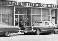 Robber exiting bank shortly before the explosion. A hostage police officer in front carries the duffel bags full of money.