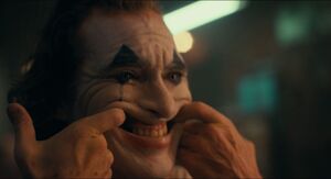 Joker forcing himself to smile by using his fingers.