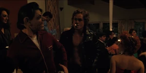 Billy smoking a cigarette as he walks past some of the party's attendees.