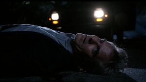 Conrad lying dead on the road after being stabbed.