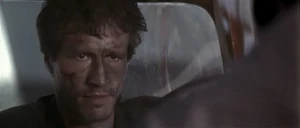 Korda attempting to escape in Scott's truck, while Scott clings to the bonnet.