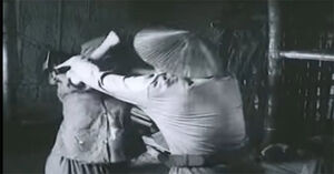 The Gaoler violently pushing Mrs. Dậu away to arrest Mr. Dậu.