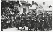 March down a street in Sanok past a swastika 1936