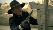 A startled Man in Black watches Teddy man the Gatling gun